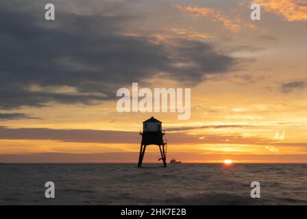 Die aufgehende Sonne wirft ein wunderschönes Gelb- und Orange-Leuchten über die Wolken und den Himmel und beleuchtet den Dovercourt Lighthouse in Harwich & Dovercourt, Großbritannien Stockfoto