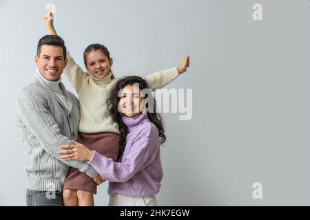 Glückliches kleines Mädchen und ihre Eltern in warmen Pullovern auf hellem Hintergrund Stockfoto