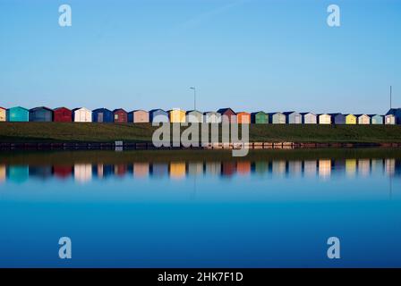 Farbenfrohe Strandhütten aus Holz säumen den Hügel entlang der Ränder des Dovercourt Bootssees entlang der North Essex Coast. Harwich & Dovercourt, England, Großbritannien Stockfoto