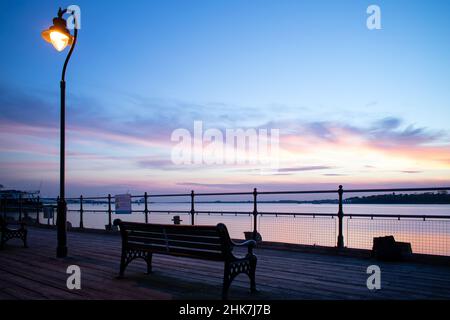 Ein wunderschöner, farbenfroher Sonnenuntergang über dem Fluss Stour, der von einer der einzigen bearbeiteten Holzpiers in Großbritannien, Ha'Penny Pier, Harwich, North Essex, aus gesehen wird. Stockfoto