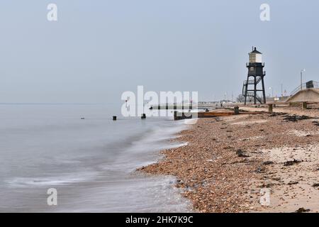 Eine lange Aufnahme von Wellen, die an einem nebligen Nachmittag am steinigen Strand vor dem Dovercourt Lighthouse brechen, Harwich & Dovercourt, Essex, Großbritannien Stockfoto