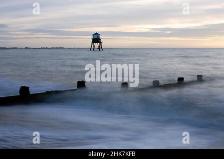 Die Wellen brechen am Strand während des Sonnenaufgangs am historischen Dovercourt Lighthouse, Harwich & Dovercourt Bay, Essex, Großbritannien Stockfoto