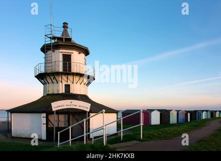 Harwich Low Lighthouse und Harwich Maritime Museum mit farbenfrohen Strandhütten entlang der Nord-Essex-Küste, wenn die Farben des Sonnenuntergangs in den Himmel eintreten. Stockfoto