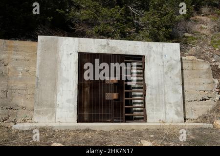 Große Tür aus Metall, Durchgang in eine Bergseite. Es gibt zwei große verriegelte Griffe. Feiner Rasterbildschirm und große Balken. Weißer Betonrahmen. Stockfoto