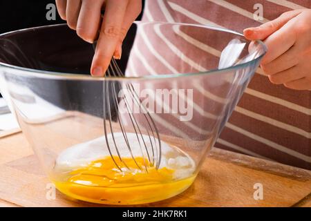 Nahaufnahme der Hände einer Frau, die Eier schlagen, um Teig auf dem Holztisch in der Küche zu machen. Hausgemachte Küche. Stockfoto
