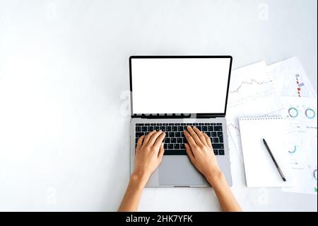 Laptop mit weißem leerem Bildschirm, Modell für Ankündigung, Werbung. Draufsicht, weibliche Hände liegen auf einer Laptop-Tastatur mit einem leeren weißen Bildschirm, ein Mädchen, das Text tippt und Informationen im Internet durchsucht Stockfoto