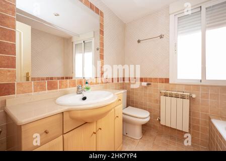 Badezimmer mit hellen Holzschränken und rötlichen und cremefarbenen Fliesen Stockfoto