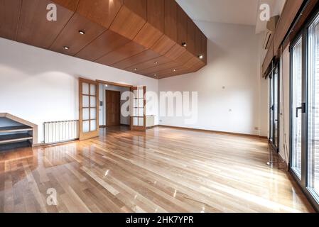 Leeres Wohnzimmer mit einem großen Bücherregal aus Eiche und langen Holzböden aus französischem Eichenfurnier in einem Loft-Penthouse mit Erkerfenstern Stockfoto