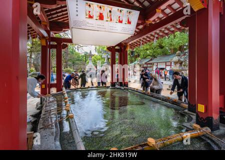 tokio, japan - 07 2019. dezember: Touristen, die sich mit Wasser in Schöpfkellen an einem Waschbecken reinigen, das von einem Explanan geschmückt wird und den Namen „temizuya“ oder „chōzuya“ trägt Stockfoto