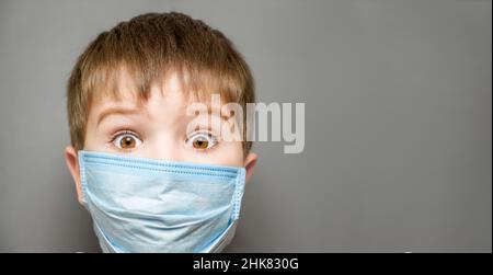 Covid 19 Kinderimpfung, Banner. Erstaunt Kind überrascht Junge trägt Maske Kind schockierte Augen weit geöffnet. Offene Augen überrascht Kind in Gesichtsmaske Kind Stockfoto