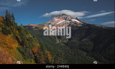 Eine linsenförmige Wolke umschließt den schneebedeckten Berg Hoot bei einem wunderschönen Sonnenuntergang im Herbst. Mit einem meist blauen Himmel gibt es eine Bergkette von Gipfeln Stockfoto