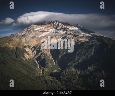 Eine linsenförmige Wolke umschließt den schneebedeckten Berg Hoot bei einem wunderschönen Sonnenuntergang im Herbst. Mit einem meist blauen Himmel gibt es eine Bergkette von Gipfeln Stockfoto