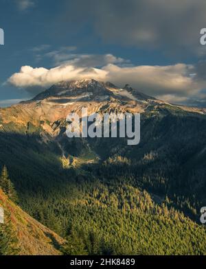 Eine linsenförmige Wolke umschließt den schneebedeckten Berg Hoot bei einem wunderschönen Sonnenuntergang im Herbst. Mit einem meist blauen Himmel gibt es eine Bergkette von Gipfeln Stockfoto