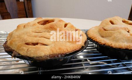 Zwei hausgemachte Apfelkuchen in Mini-Pfannen auf einem Kühlgestell über Blechfolie; Kochen und Backen zu Hause. Stockfoto