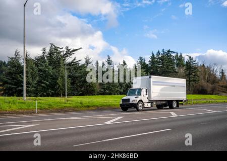 Leistungsstarker, klassischer weißer Sattelschlepper mit großem Rig, der kommerzielle Fracht in einem langen Boxanhänger für lokale Lieferungen auf dem Highway entran transportiert Stockfoto