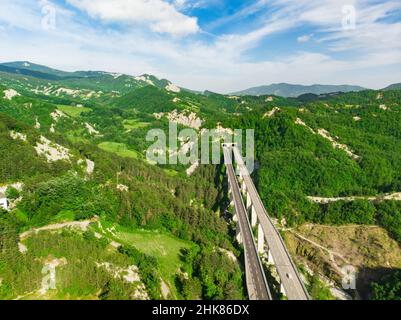 Luftaufnahme der geteilten Autobahn, die in einen Bergtunnel zwischen grünen Feldern und Hügeln um den San-Marino-Mikrostaat führt. Wir reisten über die wunderschöne Stadt Stockfoto