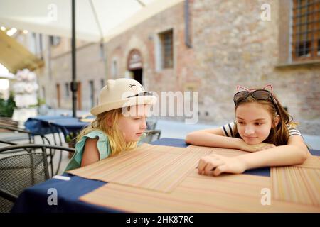 Zwei Schwestern sitzen in der Pizzeria im Freien in der alten engen Straße der berühmten Stadt Montepulciano, die sich auf einem Kalksteinkamm befindet, der von Weinbergen umgeben ist Stockfoto