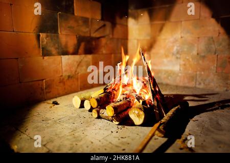 Brennendes Brennholz in der Feuerstelle des Kamins im Landhaus. Rustikaler Backofen mit brennenden Holzstämmen. Stockfoto