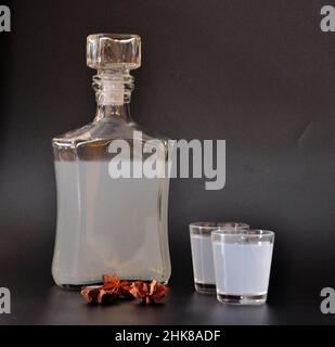Anislikör, starker selbstgemachter Alkohol, eine Flasche und zwei Gläser mit einem Getränk auf schwarzem Hintergrund, neben einem trockenen Sternaniswein. Nahaufnahme. Stockfoto