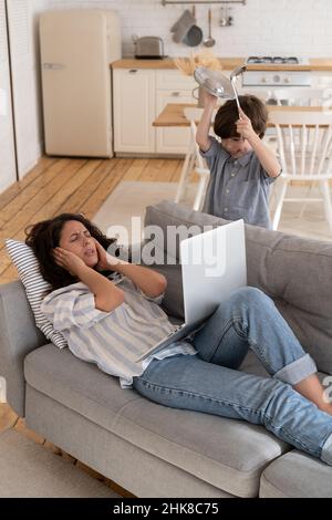 Gestresste Mutter schauen verzweifelt auf laute Kind leiden unter Kopfschmerzen. Mama ist durch schlechtes Verhalten des Sohnes verarkt Stockfoto