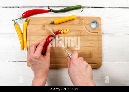 Frauenhänden mit einem Messer schneiden Pfeffer auf einem Bambusschneidebrett. Gewürze und Bio-Produkte. Stockfoto