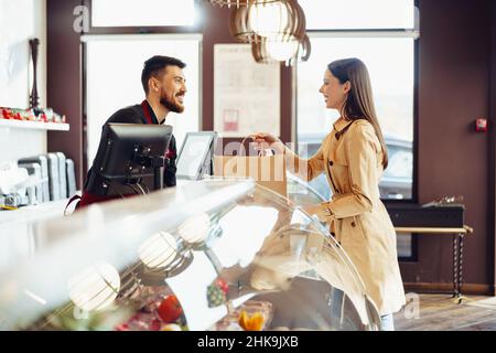 Verkäuferin, die Einkaufstasche an weibliche Kundin im Lebensmittelgeschäft abgibt Stockfoto