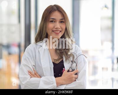Porträt einer eleganten asiatischen Ärztin in weißem Mantel steht mit gekreuzten Armen und Stethoskop. Arzt, medizinische Arbeit Stockfoto