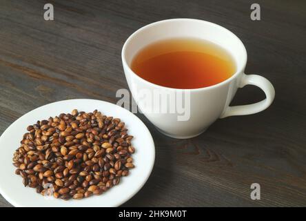 Teller mit gerösteter Gerste mit einer Tasse heißen japanischen Gerstentee oder Mugicha auf schwarzem Holztisch Stockfoto