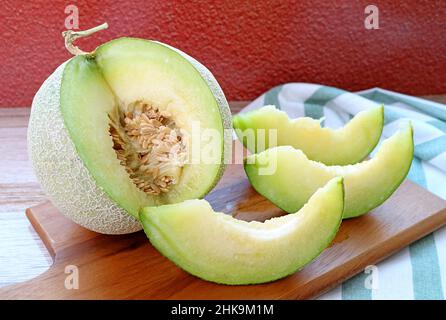 Scheiben frischer reifer süßer und aromatischer Muskmelone mit ganzen Früchten auf Holzschneidebret Stockfoto