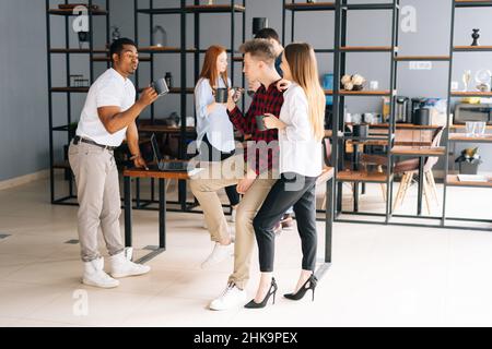 Eine Gruppe von fünf erfolgreichen jungen, multiethnischen Start-up-Kollegen aus Unternehmen, die während der Kaffeepause im Co-Working-Bereich angenehme Gespräche führen. Stockfoto