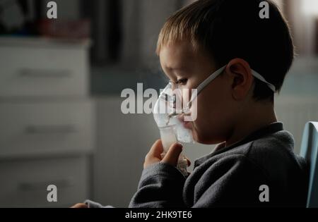 Behandlung zu Hause. Der Junge atmet mit einem Vernebler ein und inhaliert Medikamente in seine Lungen. Selbstbehandlung der Atemwege mit Inhalation. Stockfoto