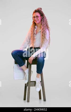 Frau mit Dreadlocks sitzt auf einem hohen Stuhl und hält ein Magazin in der Hand Stockfoto