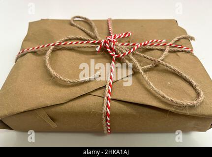 Geschenk verpackt mit Normalpapier und gebunden mit roten und braunen Schnur Stockfoto