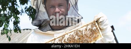 Imker im Schutzanzug hält Waben mit Bienen Stockfoto