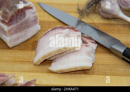 Ukrainische Produkte rohen Schmalz mit Pfefferkorn und Knoblauch, Messer, Scheiben von salo auf Schneidebrett. Traditionelles ukrainisches Lebensmittelkonzept. Stockfoto