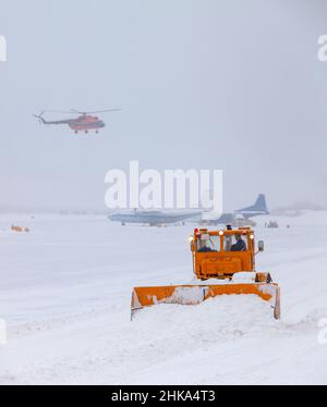 Der Schneepflug reinigt nach starkem Schneesturm auf der Piste. Der Hubschrauber landet bei schlechtem Wetter, bei starkem Schneefall. Der Transporttransp Stockfoto