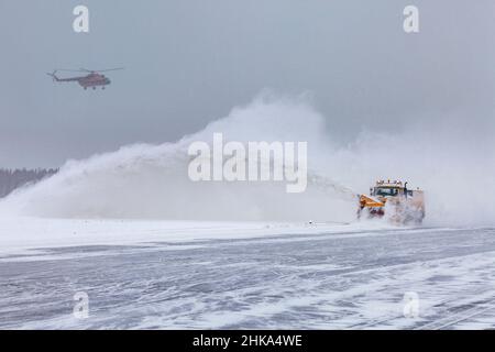 Der Schneepflug reinigt nach starkem Schneesturm auf der Piste. Der Hubschrauber landet bei schlechtem Wetter, bei starkem Schneefall. Stockfoto