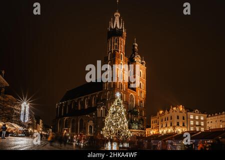 Krakau, Polen-Dezember 17,2021. Basilika der Heiligen Maria und berühmten Weihnachtsmarkt auf dem Hauptplatz, Rynek Glowny in der Nacht, dekoriert Holzhütten und Weihnachten Stockfoto