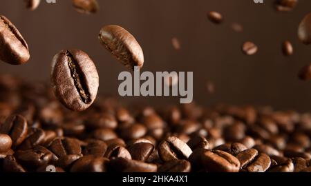 Geröstete, heiße Kaffeebohnen fallen auf einen Haufen Kaffeebohnen. Vorderansicht. Horizontale Zusammensetzung. Stockfoto