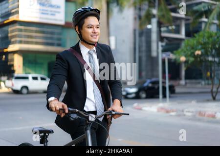 Ein asiatischer Geschäftsmann schiebt morgens sein Fahrrad von zu Hause und bereitet sich darauf vor, mit dem Fahrrad zur Arbeit zu fahren. Umweltfreundlicher Transport. Stockfoto
