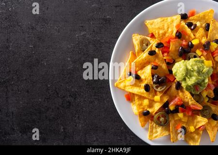 Mexikanische Nachos-Tortilla-Chips mit schwarzen Bohnen, Guacamole, Tomaten und Jalapeno auf schwarzem Hintergrund Stockfoto