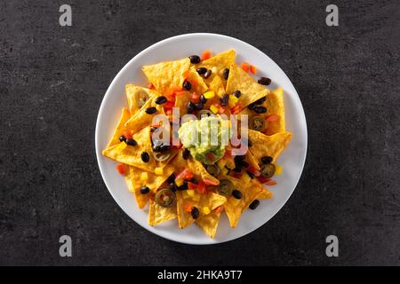 Mexikanische Nachos-Tortilla-Chips mit schwarzen Bohnen, Guacamole, Tomaten und Jalapeno auf schwarzem Hintergrund Stockfoto