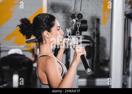 Seitenansicht der Sportlerin aus dem Nahen Osten, die im Fitnessstudio mit einem lat-Pulldown-Gerät trainieren kann Stockfoto