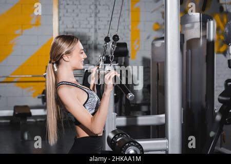 Seitenansicht der jungen Sportlerin mit Hantel beim Ausarbeiten mit lat-Pulldown-Maschine im Sportzentrum Stockfoto