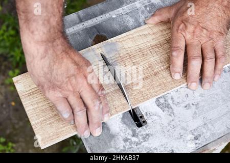 Ein Mann schneidet eine Keramikfliesen mit einem Fliesenschneider mit Wasserkühlung. Nahaufnahme, selektiver Fokus Stockfoto