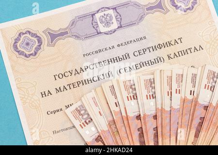 Text Russische Föderation Staatliche Bescheinigung über Mutterschaftskapital und viele Geldscheine fünftausend. Staatliche Unterstützung für die Familie bei der Geburt von seco Stockfoto