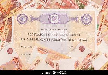 Text Russische Föderation Staatliche Bescheinigung über Mutterschaftskapital und viele Geldscheine fünftausend. Staatliche Unterstützung für die Familie bei der Geburt von seco Stockfoto