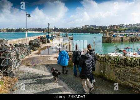 Eine Familie von Urlaubern und ihrem Hund, die zum North Quay im malerischen, funktionierenden Hafen in Newquay in Cornwall wandern. Stockfoto