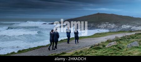 Ein Panoramabild von Menschen, die bei stürmischen Wetterbedingungen den Küstenpfad entlang über die zerklüftete Küste von Towan Head in Newquay in Cornwall wandern. Stockfoto