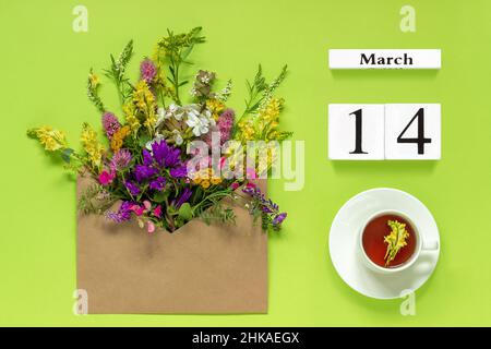 Holzwürfel Kalender März 14. Tasse Kräutertee, Kraftumschlag mit bunten Blumen auf grünem Hintergrund. Concept Hello Spring Creative Top vie Stockfoto